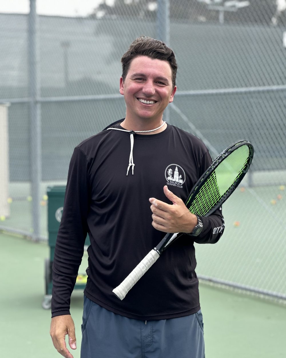 An HJK coach courtside at Balboa, racket in hand, between drills