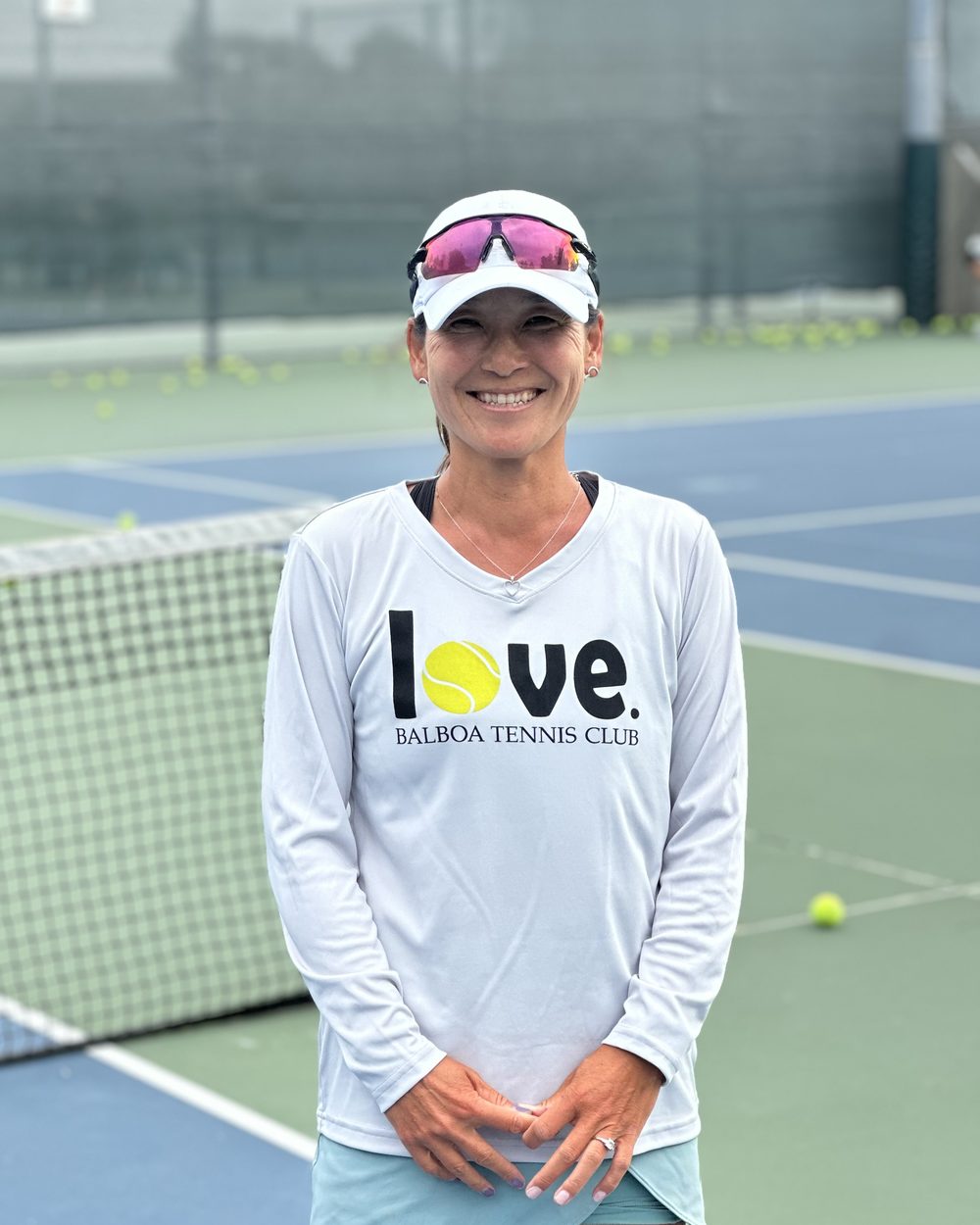 A smiling player in a Balboa Tennis Club shirt standing at the net